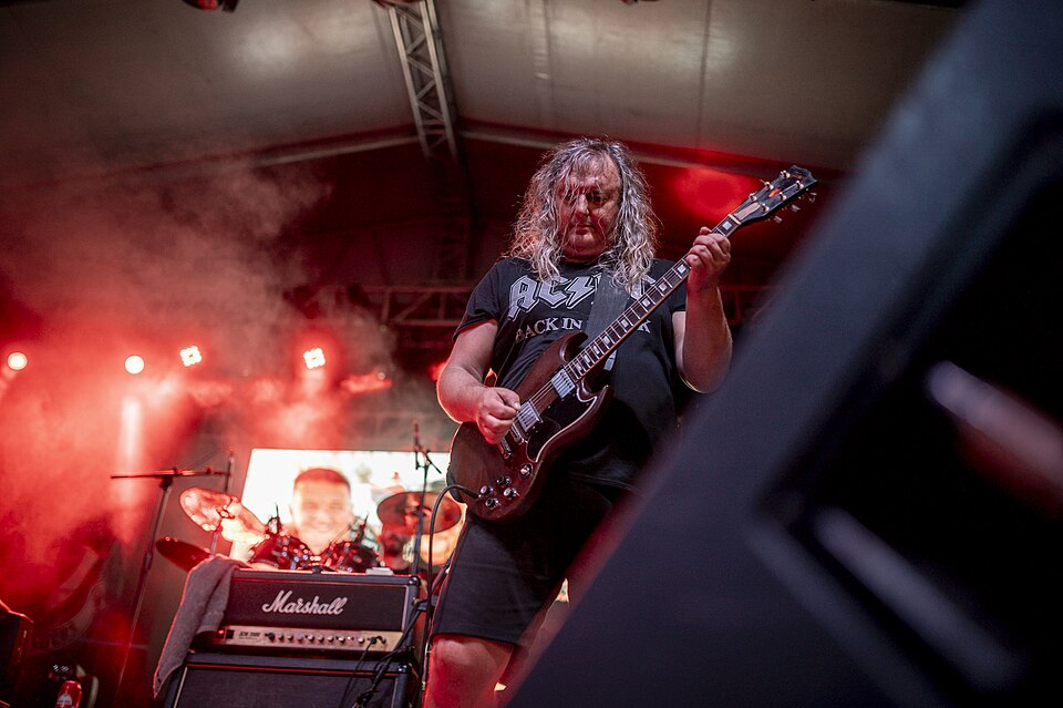Rock band performs at outdoor festival with vibrant lighting and enthusiastic crowd